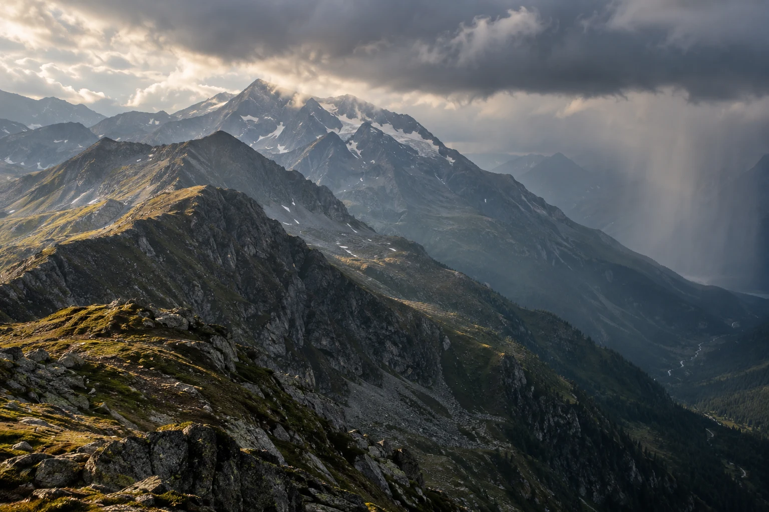 Rocky mountain ridges with warm patches of grass beneath dark clouds and a distant rain curtain.