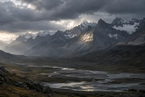 Wide rocky mountain valley with winding silver water and a patch of sunlight on a tall ridge.