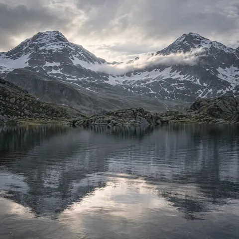 Two snow-striped mountain shoulders and their softened reflections in a gray alpine lake.