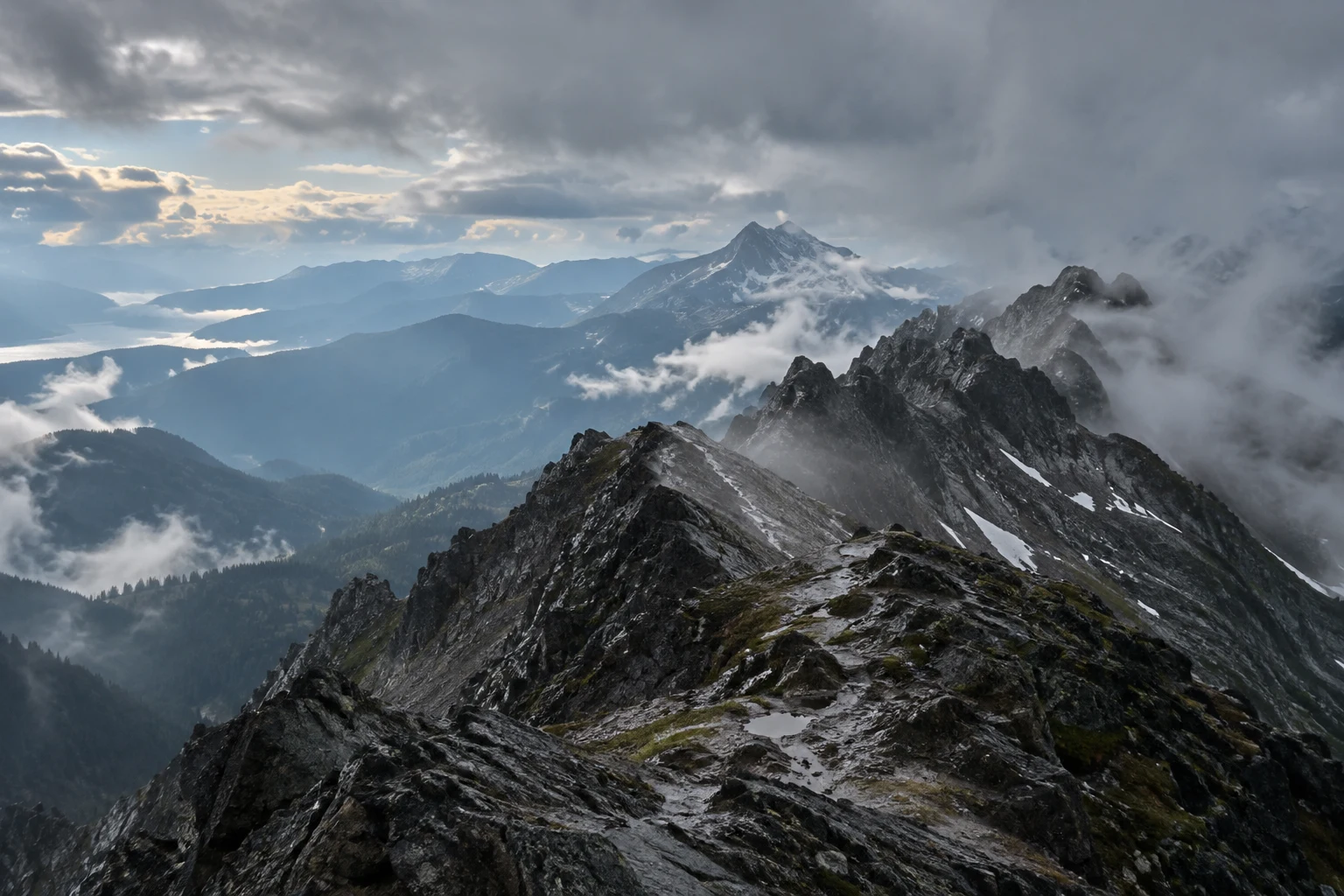 Wet jagged ridge above forested mountain layers with lifting white clouds.