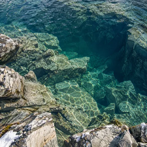 Overhead view into clear alpine water with pale fractured rock shelves and a deep blue hollow.
