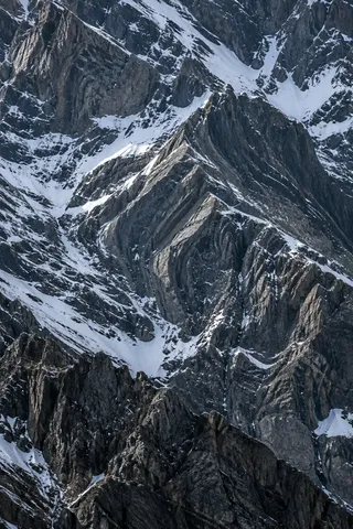 Close portrait of angular dark mountain rock divided by irregular white snow channels.