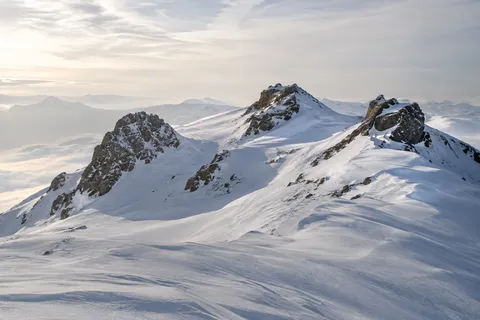 Snow-covered mountain ridge with three dark rock outcrops and pale winter light.