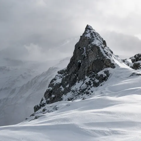Single triangular dark mountain outcrop surrounded by gently wind-shaped snow.