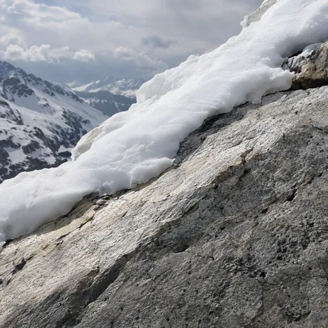 Close diagonal pale granite slab topped by granular snow, with soft distant snowy mountains.