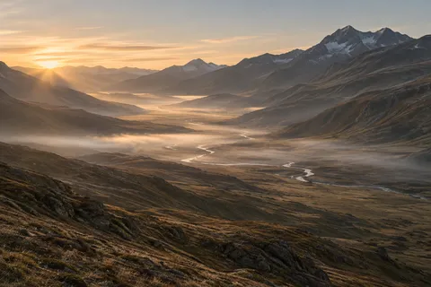 Long brown mountain valley with a winding silver river and low mist illuminated by dawn.