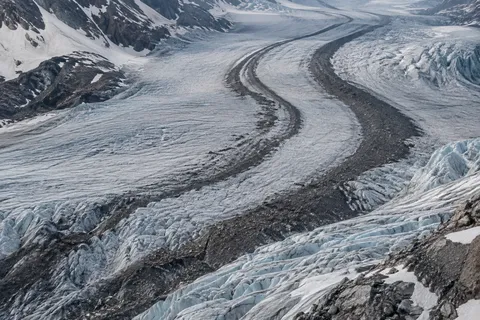 Elevated view of a glacier with two dark curved debris bands and rough blue-white ice.