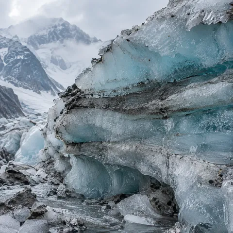 Close blue-white glacier ice cross-section with dark sediment layers and rough broken edges.