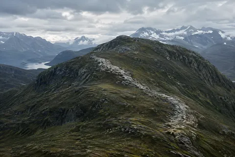 Broad rocky foothill with an exposed pale diagonal seam, distant snowy mountains and a small lake at left.