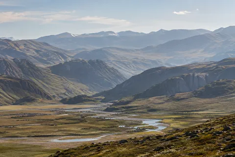 Wide olive and brown mountain valley with a winding silver river, low rocky foreground and progressively paler distant hills.
