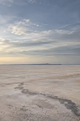 Pale flat salt basin with an irregular dark foreground seam beneath a broad blue-gray clouded sky.