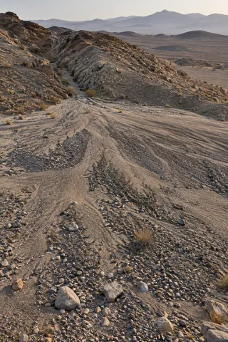 Gravel and silt fan spreading from a narrow dry channel over pale desert ground.