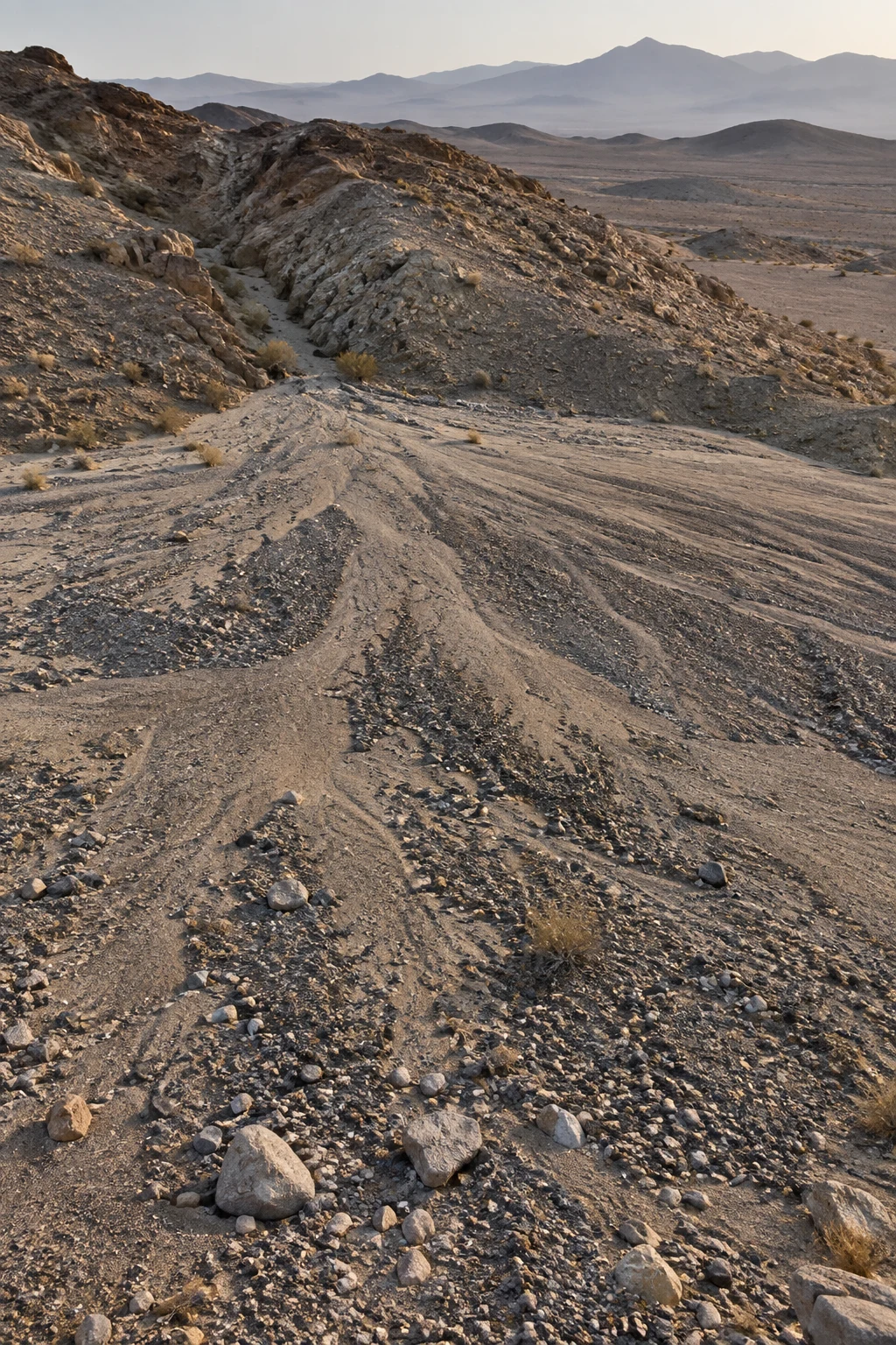 Gravel and silt fan spreading from a narrow dry channel over pale desert ground.