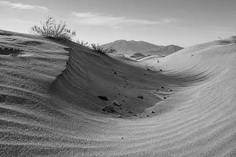 Black-and-white sand trough with a sharp left edge, rounded right bank, small stones, and distant hills.