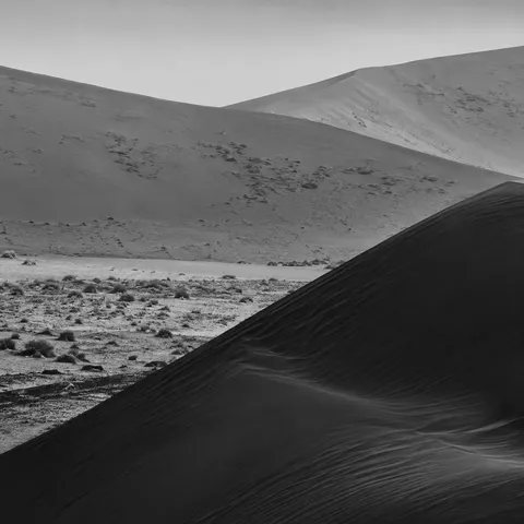 Black-and-white dark dune shoulder crossing diagonally in front of pale distant sand slopes.