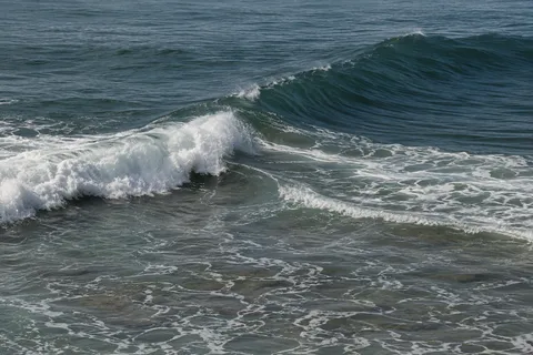Intersecting dark swells and white breakers form diagonals across a textured sea.