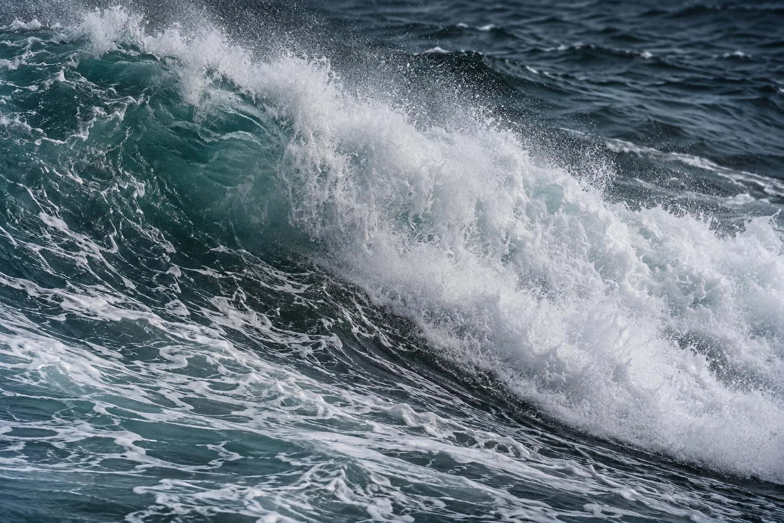 Heavy whitewater sweeps across a dark teal wave in a close diagonal view.