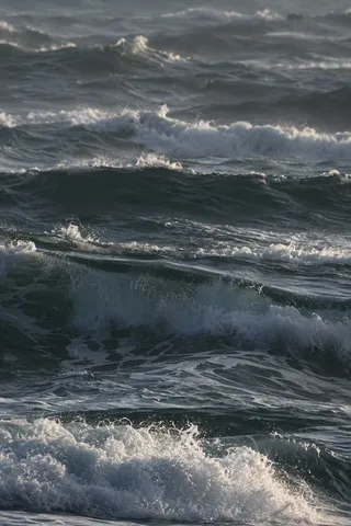Stacked dark swells and bright foam fill a narrow vertical view of the sea.