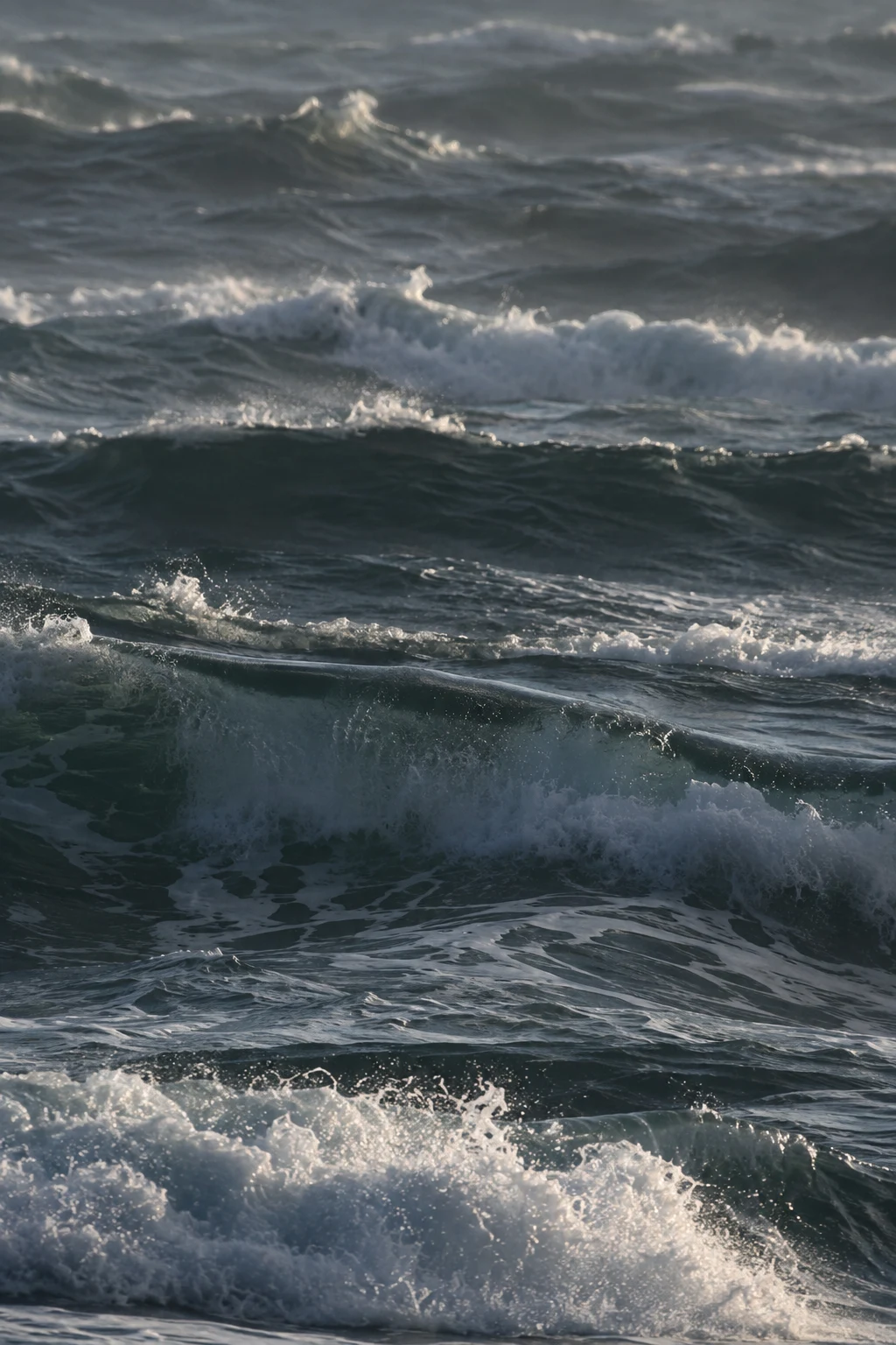 Stacked dark swells and bright foam fill a narrow vertical view of the sea.