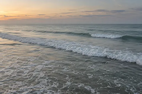 Two low surf fronts cross shallow water below a softly colored dawn sky.