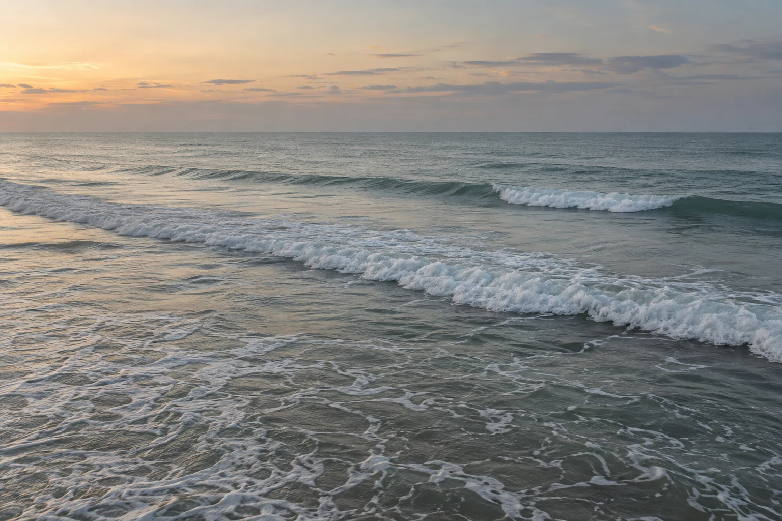 Two low surf fronts cross shallow water below a softly colored dawn sky.