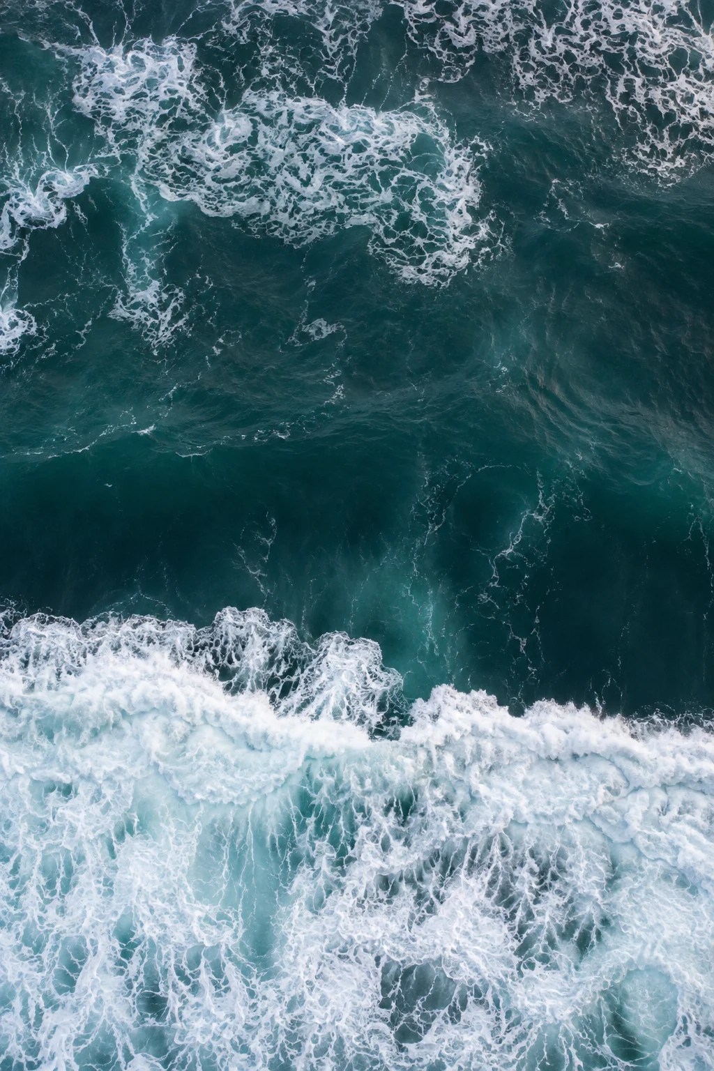A dark blue-green interval separates fresh whitewater from a finer floating foam pattern.