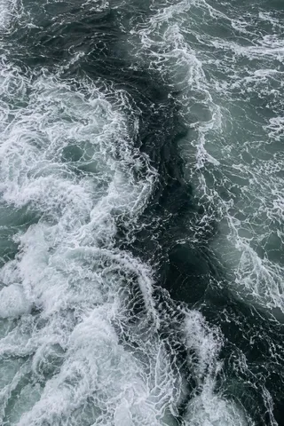 A dark winding channel cuts through pale foam on gray-green water.