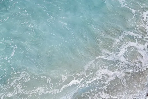 Delicate foam spreads along the edge of milky blue shallows around a quiet open center.