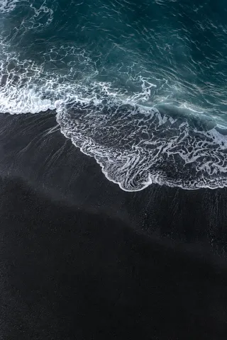 A thin white wave fans across an empty black-sand beach below dark blue water.