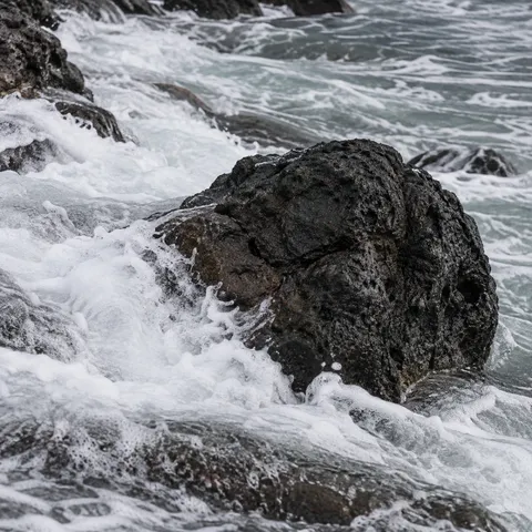 A rough dark boulder rises through rushing white surf.