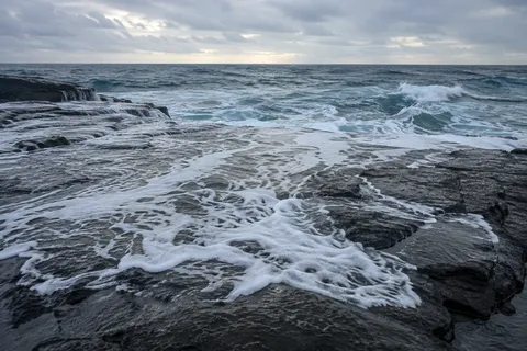 A thin sheet of white surf spreads across a broad dark rock shelf.