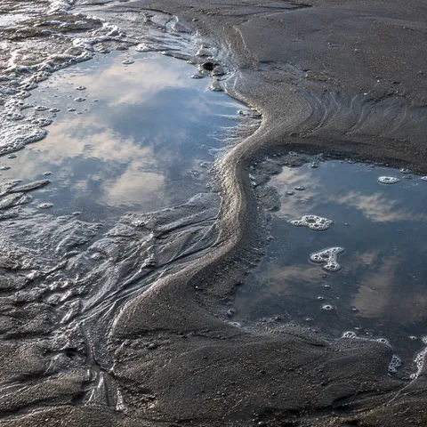 Two shallow pools reflect clouds beside a winding ridge of dark wet sand.