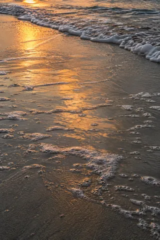 Amber light glows across shallow backwash and small foam patches on wet sand.