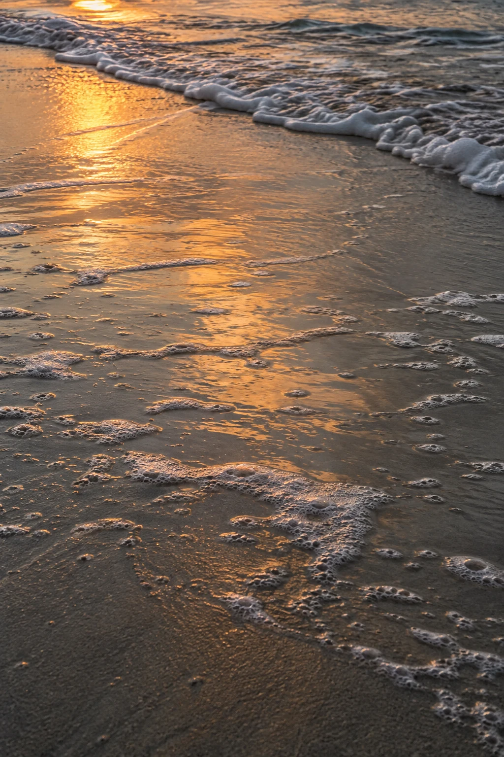Amber light glows across shallow backwash and small foam patches on wet sand.