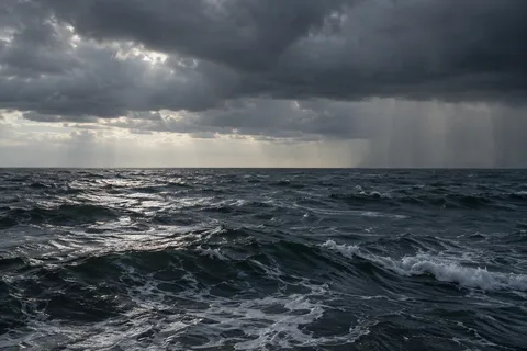 Dark rolling water lies beneath a low storm cloud and a distant curtain of rain.