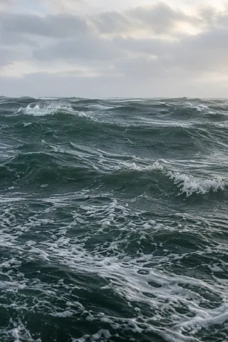 Short green-gray waves lift white crests beneath a pale clouded sky.