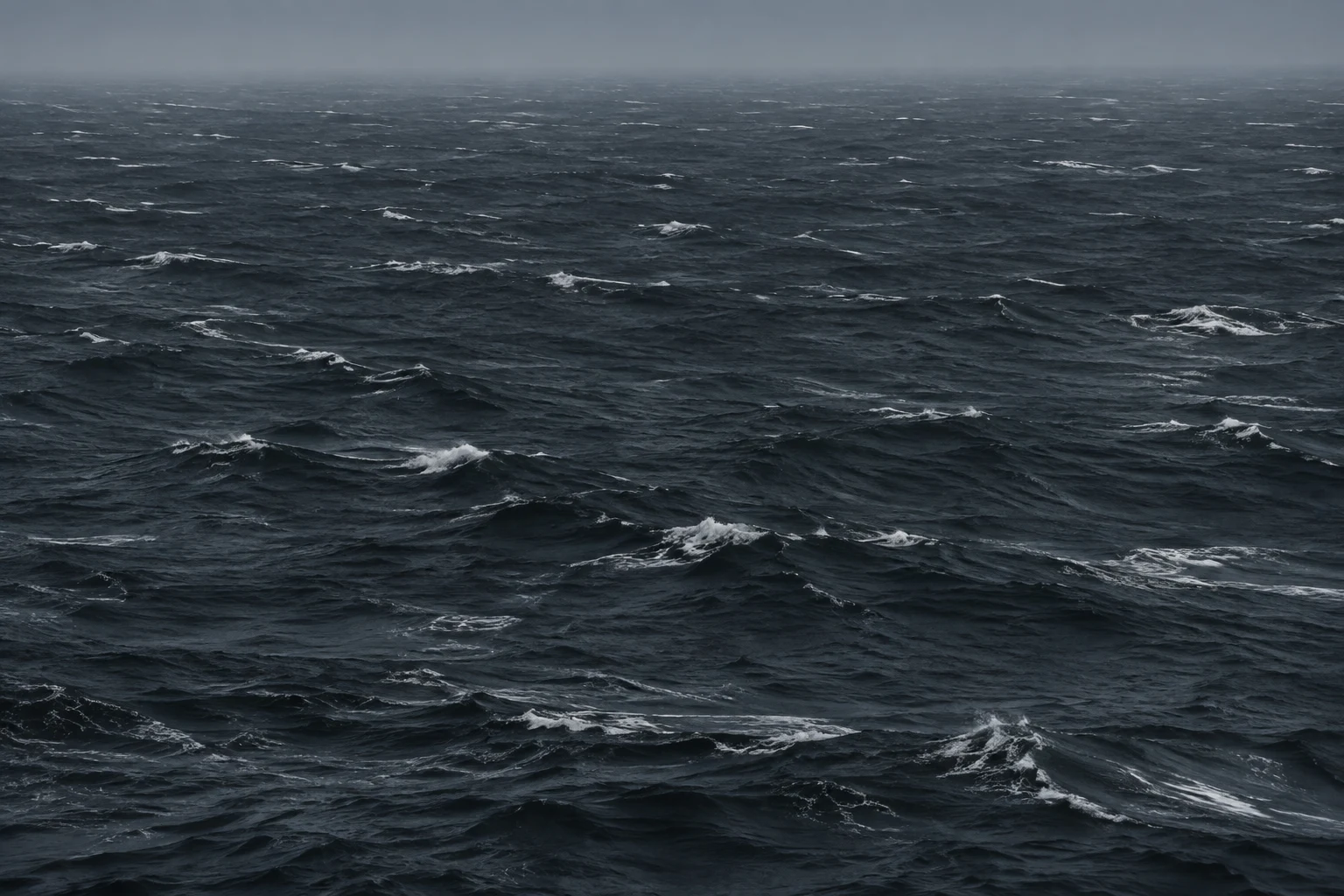 Small whitecaps scatter across dark charcoal water beneath a misty horizon.
