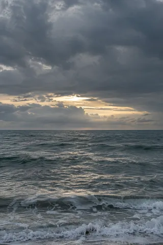 A narrow bright opening appears under heavy clouds above a choppy sea.