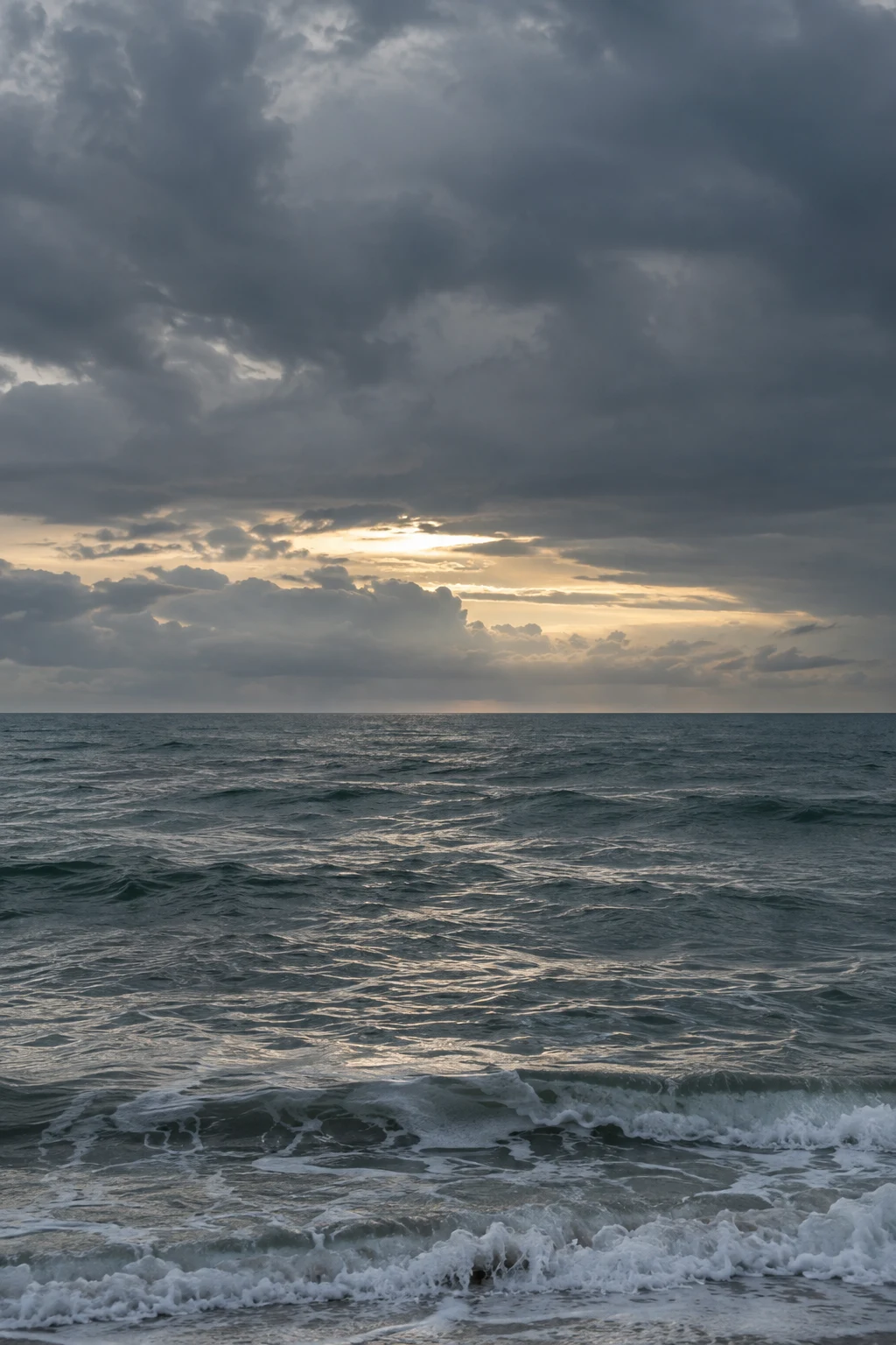 A narrow bright opening appears under heavy clouds above a choppy sea.