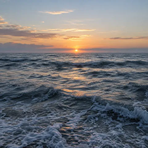 A low golden sun lights silver-blue waves beneath scattered dawn clouds.