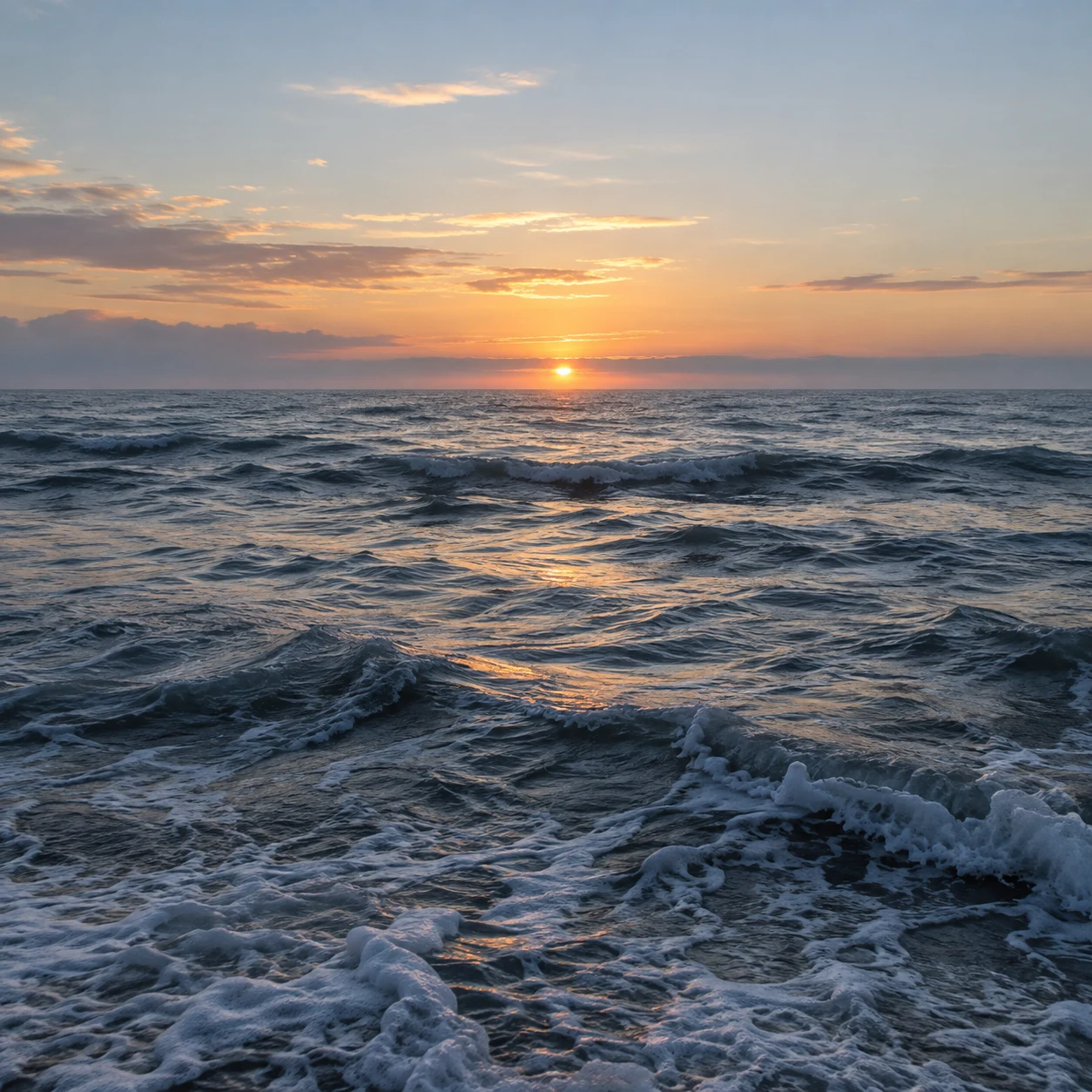 A low golden sun lights silver-blue waves beneath scattered dawn clouds.