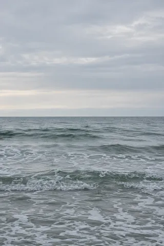 Small gray-green breakers roll beneath a broad pale winter sky.