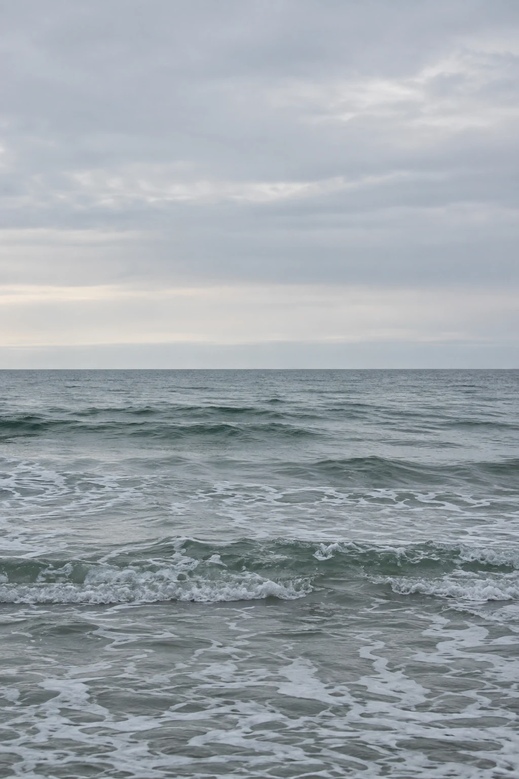 Small gray-green breakers roll beneath a broad pale winter sky.