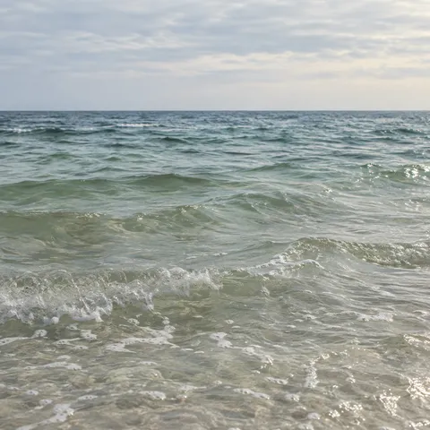 Clear pale green wavelets ripple toward a distant blue-gray horizon under thin cloud.