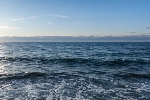 Dark blue waves sit below a clearing blue sky and a low horizontal ribbon of gray cloud.