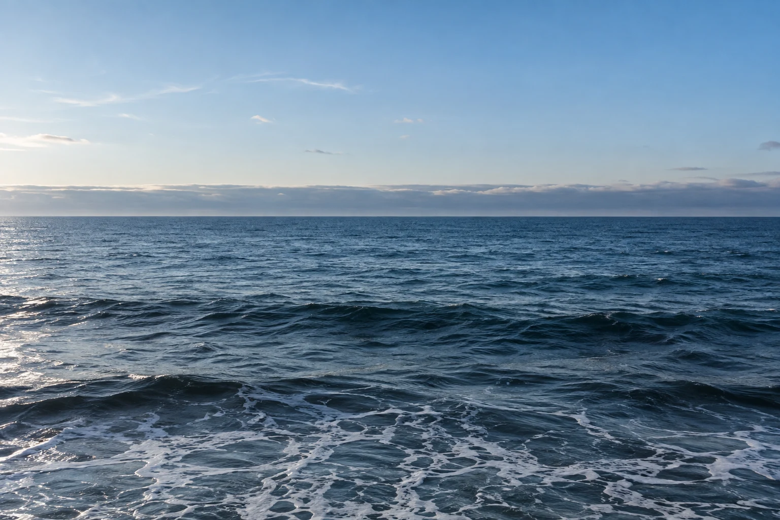 Dark blue waves sit below a clearing blue sky and a low horizontal ribbon of gray cloud.