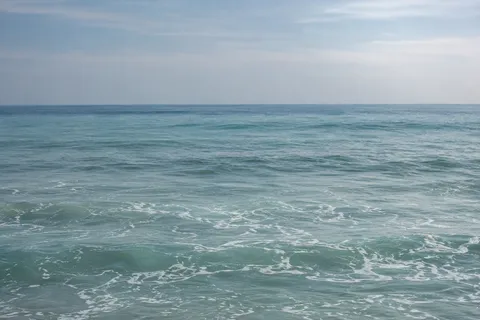Pale teal water and fine foam soften into blue distance under a hazy sky.