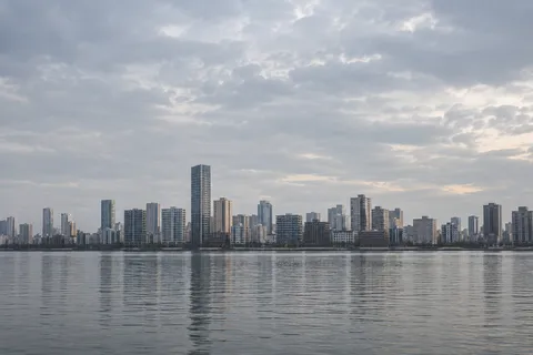 Pale rectangular waterfront towers and their broken reflections beneath an expansive gray sky.