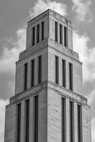 A close upward view of a stepped pale stone tower with narrow dark windows and simple cornices.