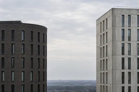 Dark rounded brick architecture at left and pale concrete architecture at right with a distant low horizon between.